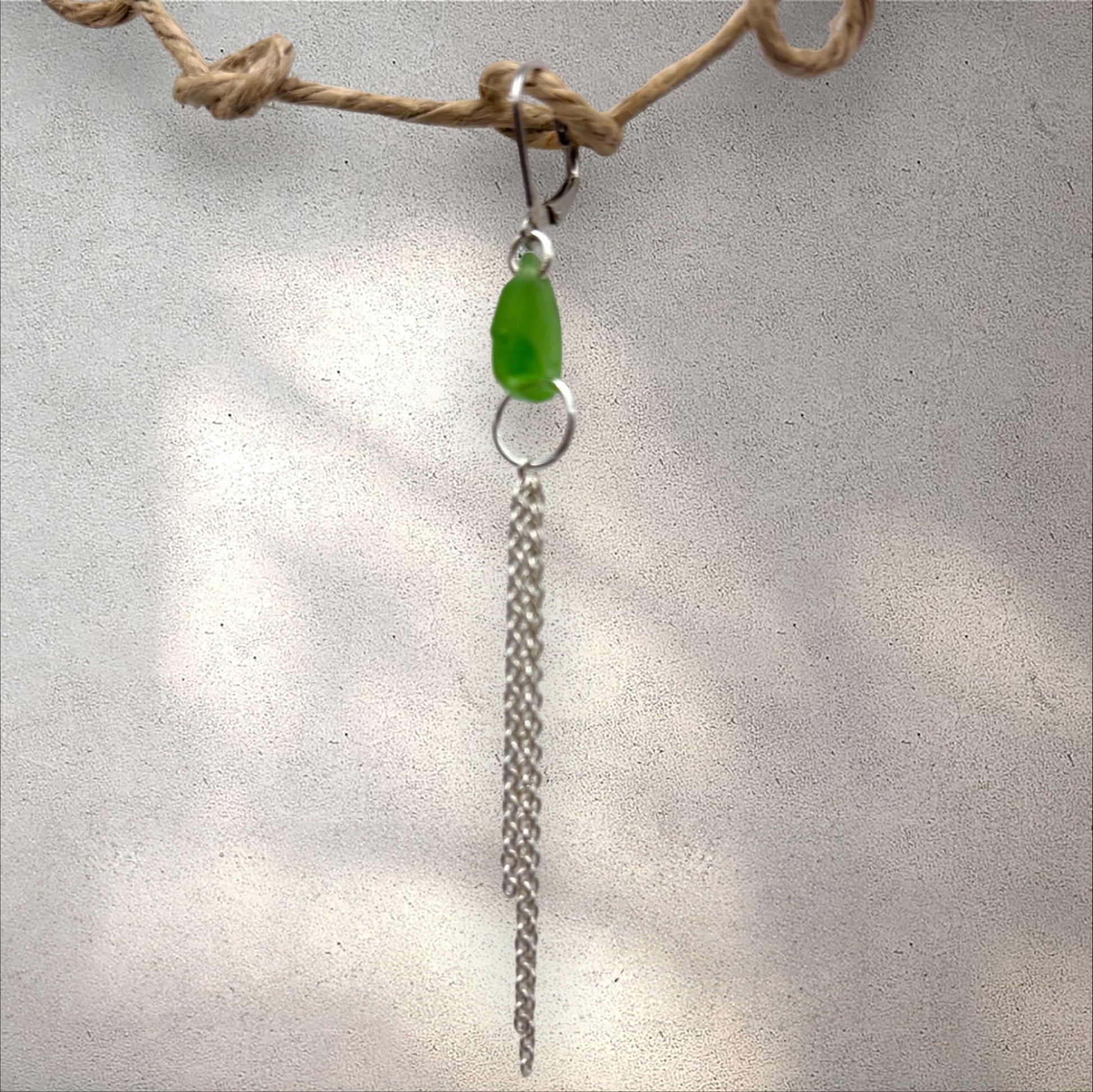 earring with a green sea glass and silver chain on a textured surface