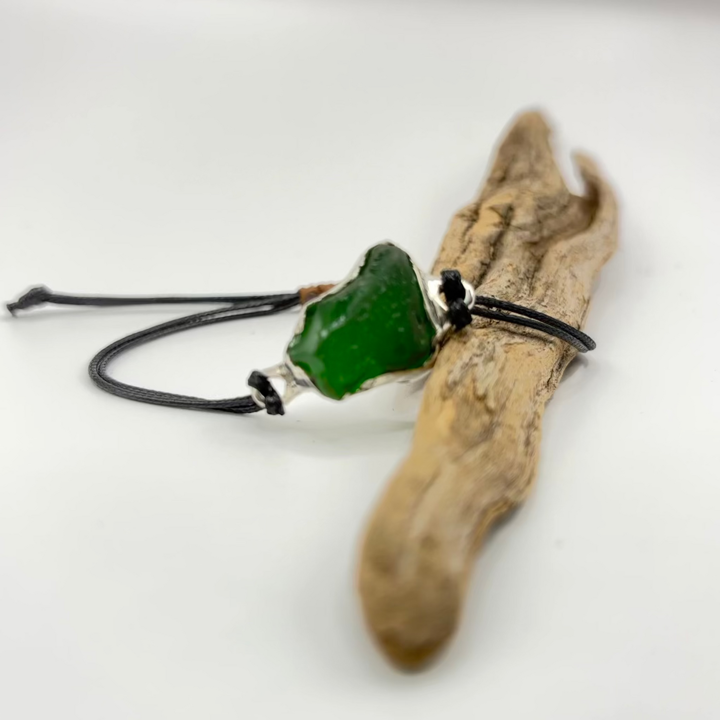 bracelet with green pendant on a piece of driftwood against a white background