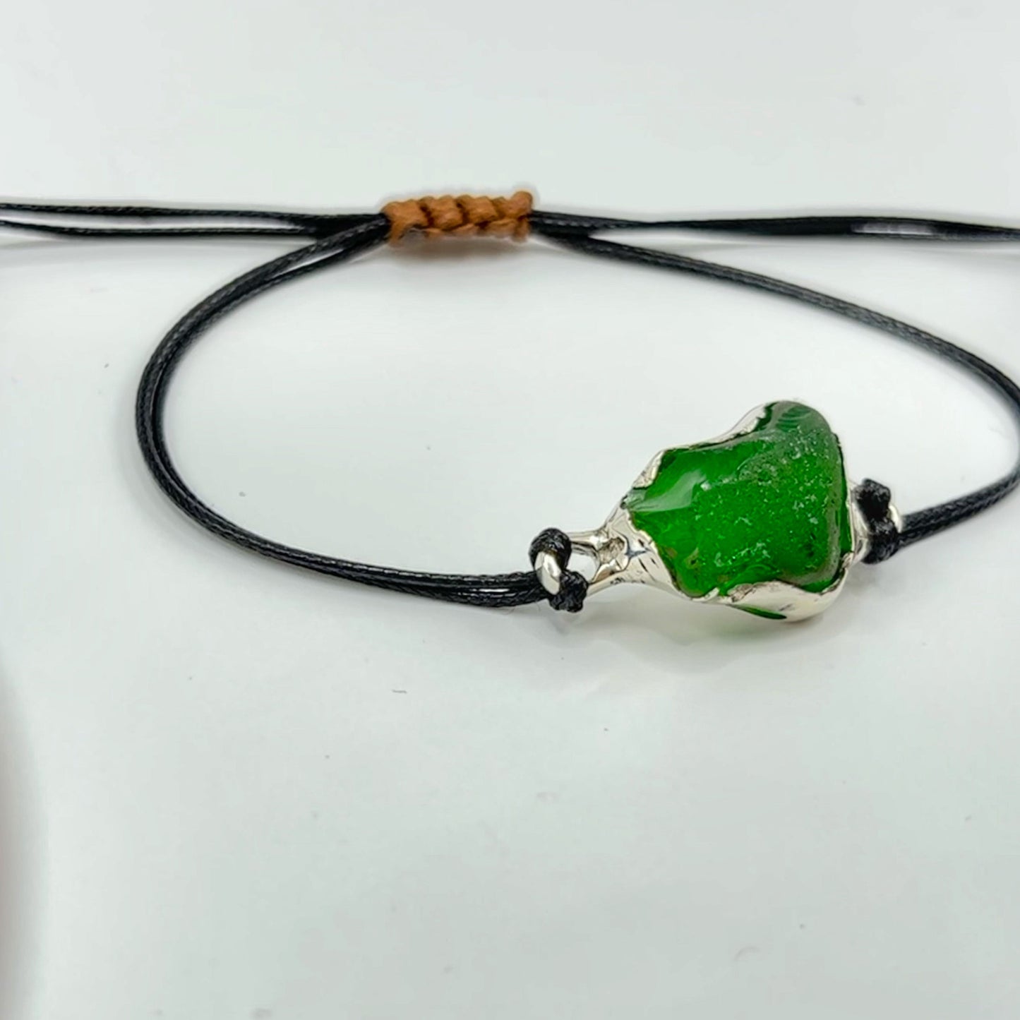 Green sea glass bracelet on a black cord against a white background
