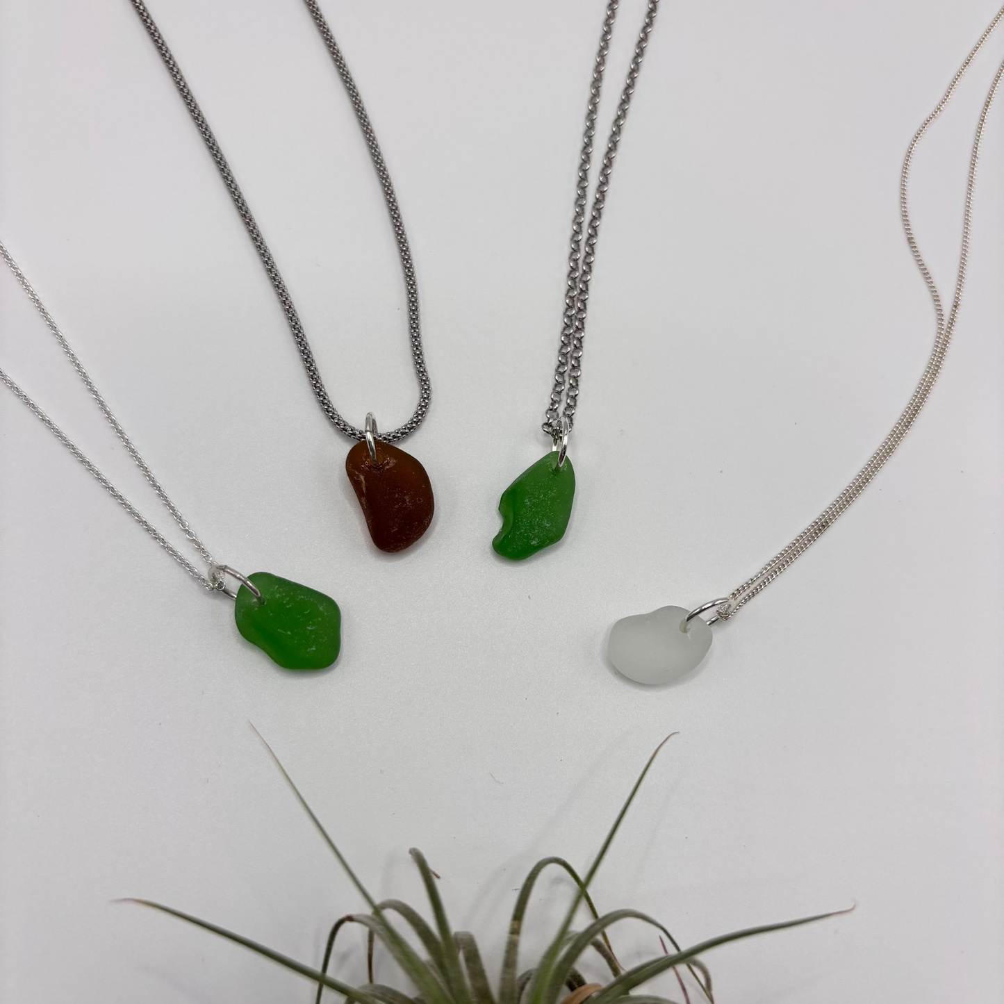 four sea glass pendants set in silver on a silver chain, with soft sea-shaped edges and a natural glow.