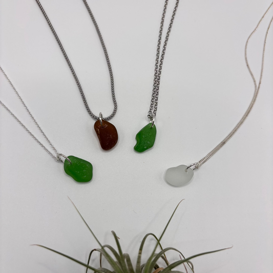 four sea glass pendants set in silver on a silver chain, with soft sea-shaped edges and a natural glow.