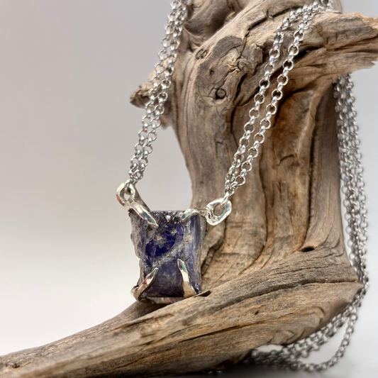 Silver necklace with a tanzanite raw stone pendant on a wooden branch. hand made
