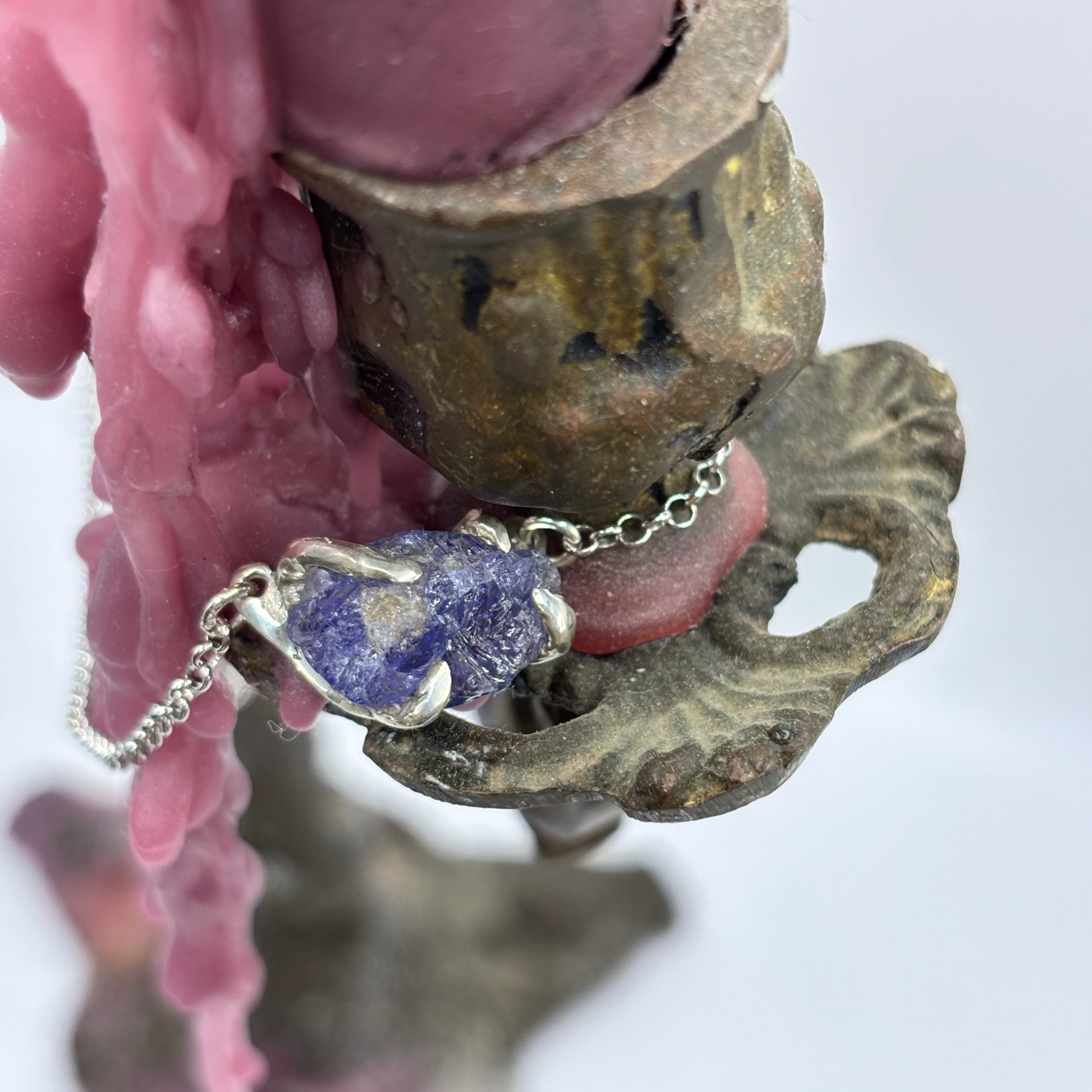 Raw tanzanite stone held in silver claws, crafted with the lost wax technique, showing deep violet and blue tones, suspended on a silver chain with four silver claws.